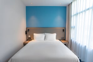 A hotel room with a large bed, a nightstand, a bedside table, and a window with curtains. - Holiday Inn Express Shantou City Center by IHG (Shantou)