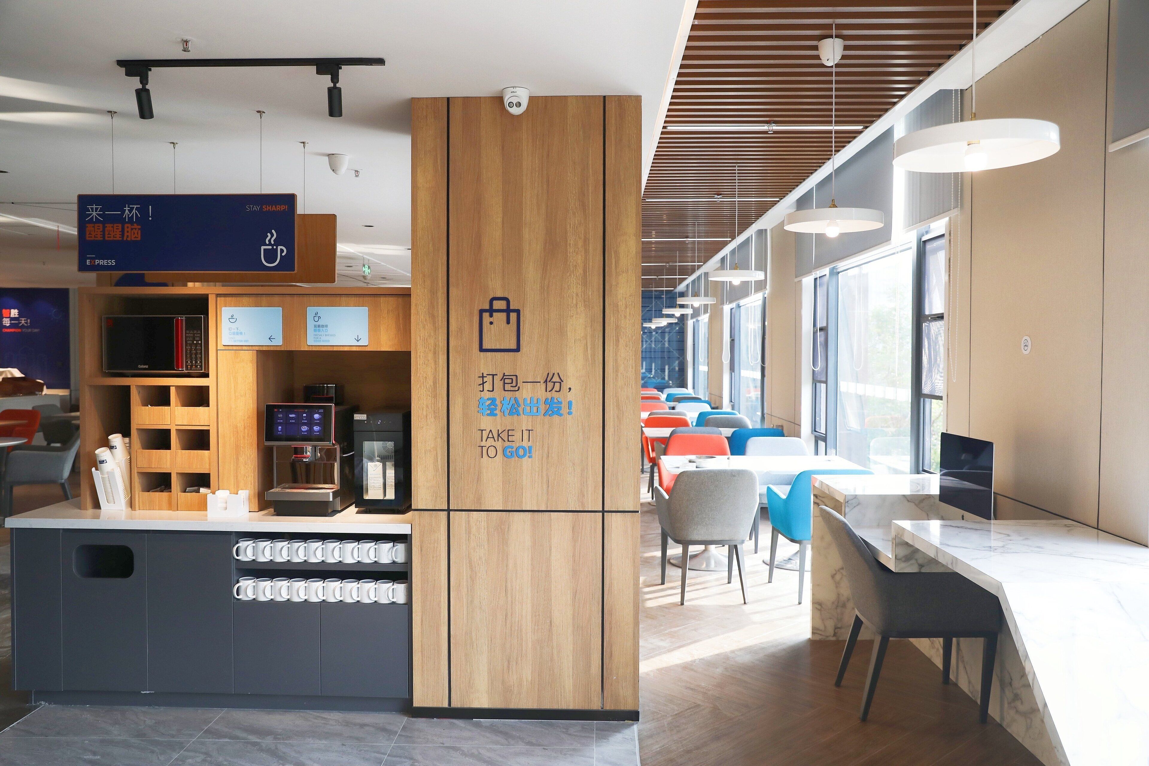Una cafetería moderna con mostrador de madera, una máquina de café digital y un cartel animando a los clientes a llevar una taza.