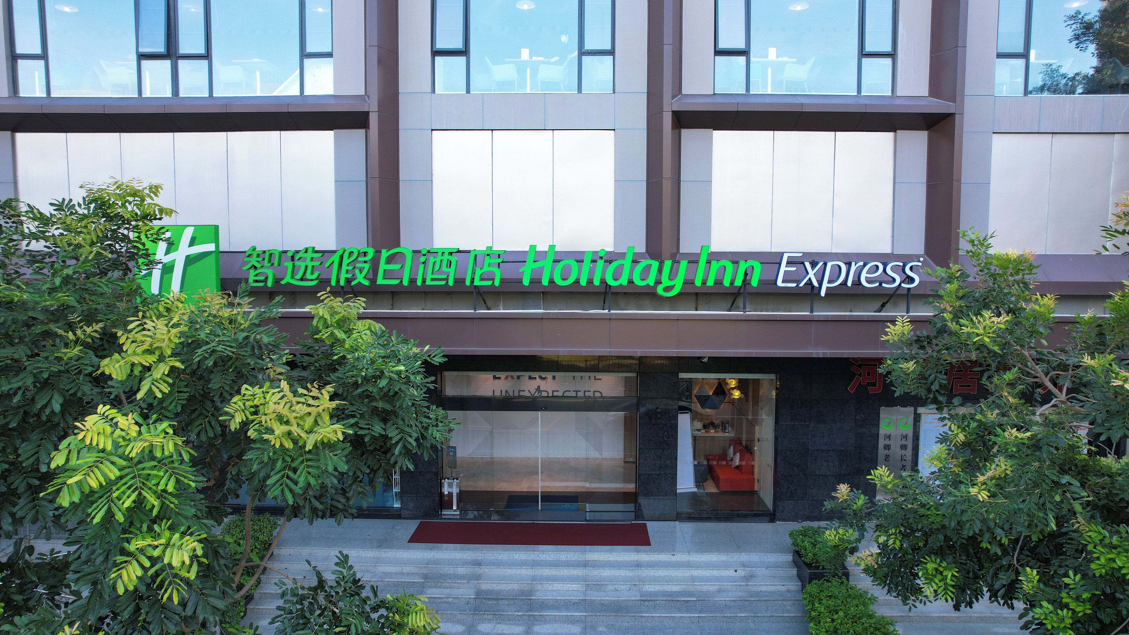 Un bâtiment de l’hôtel Holiday Inn Express doté d’une façade moderne, de grandes fenêtres et d’un tapis rouge menant à l’entrée.