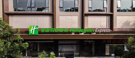 A hotel facade with a green logo, signage in multiple languages, and a modern architectural design.