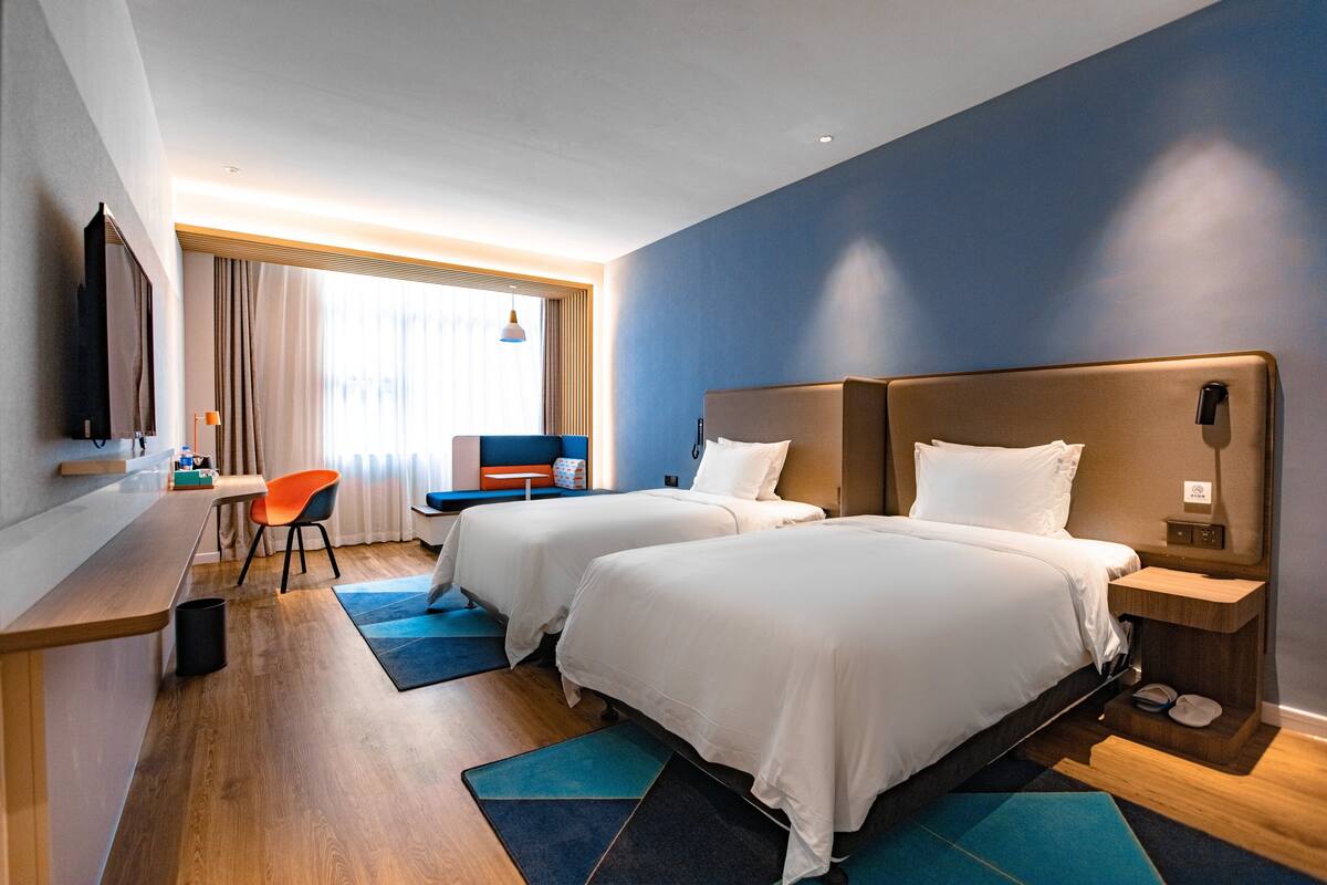 Ein Hotelzimmer mit zwei Betten, einem Schreibtisch, einem Stuhl und einem Fernseher.