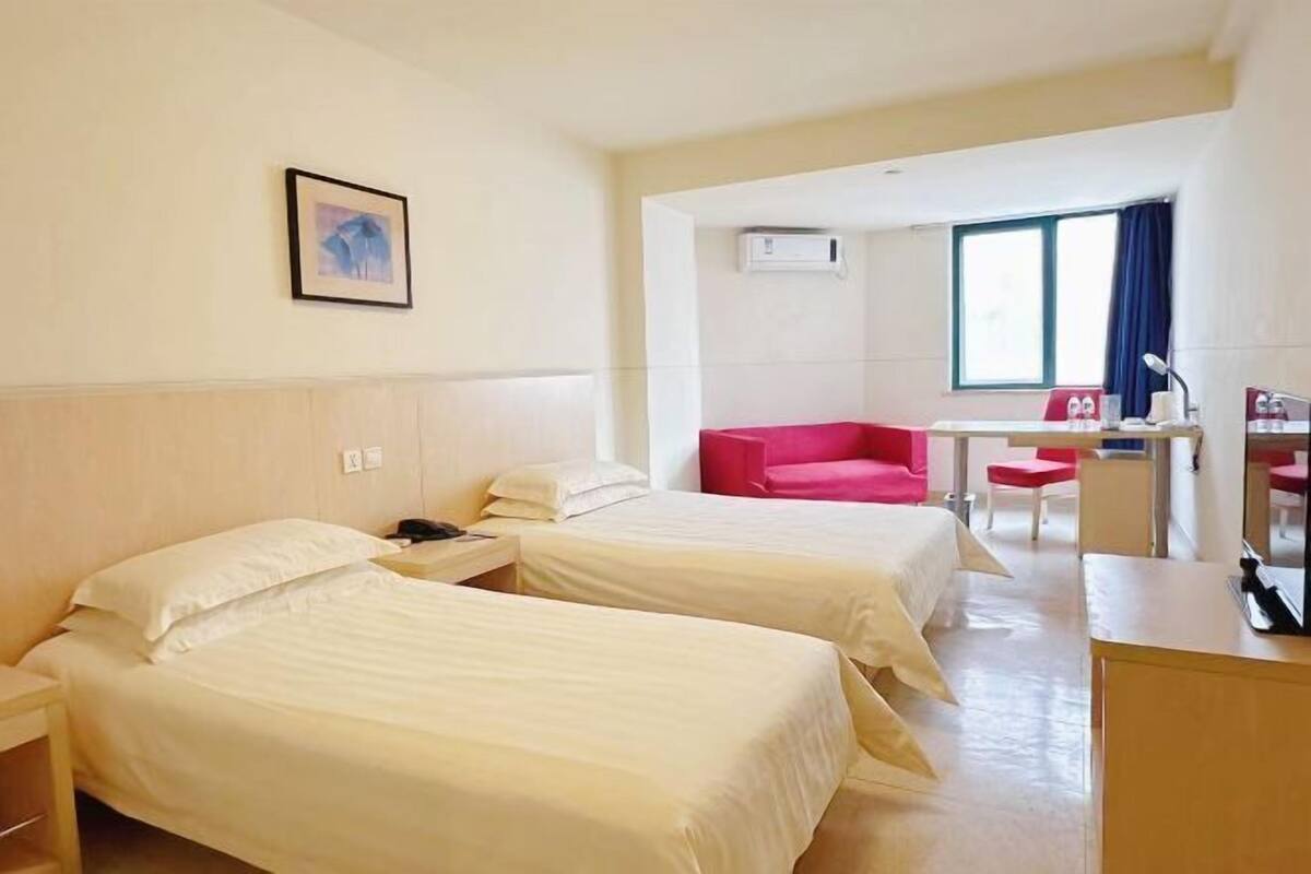Een hotelkamer met twee bedden, een bureau, een stoel en een raam met gordijnen.