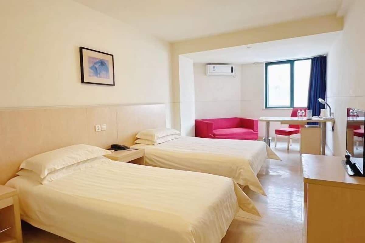 A hotel room with two beds, a desk, a chair, and a window with curtains.