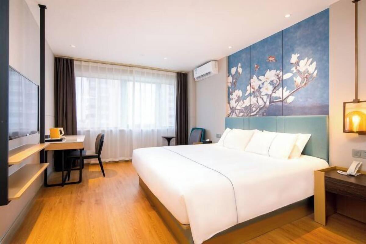 Hotelkamer met een groot bed, bureau met stoel, televisie en schilderij aan de muur.