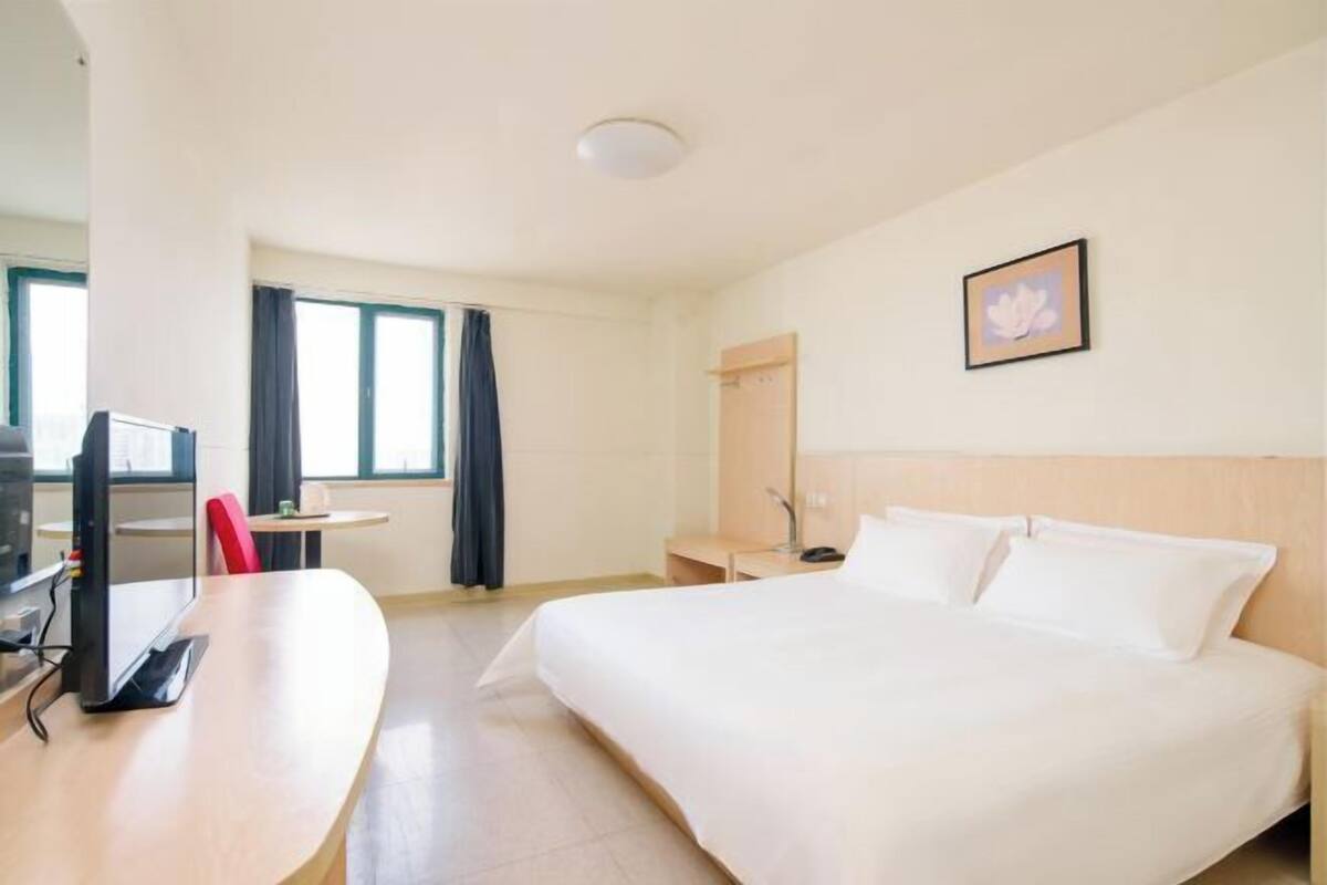 Hotelkamer met een bed, bureau met computer, stoel, klein tafeltje en raam met gordijnen.