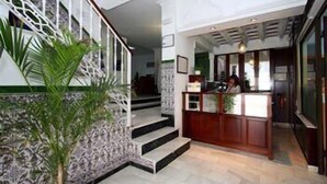 A reception area with a wooden desk, a staircase with a patterned wall, and a potted plant. - Hotel Oasis (Conil de la Frontera)