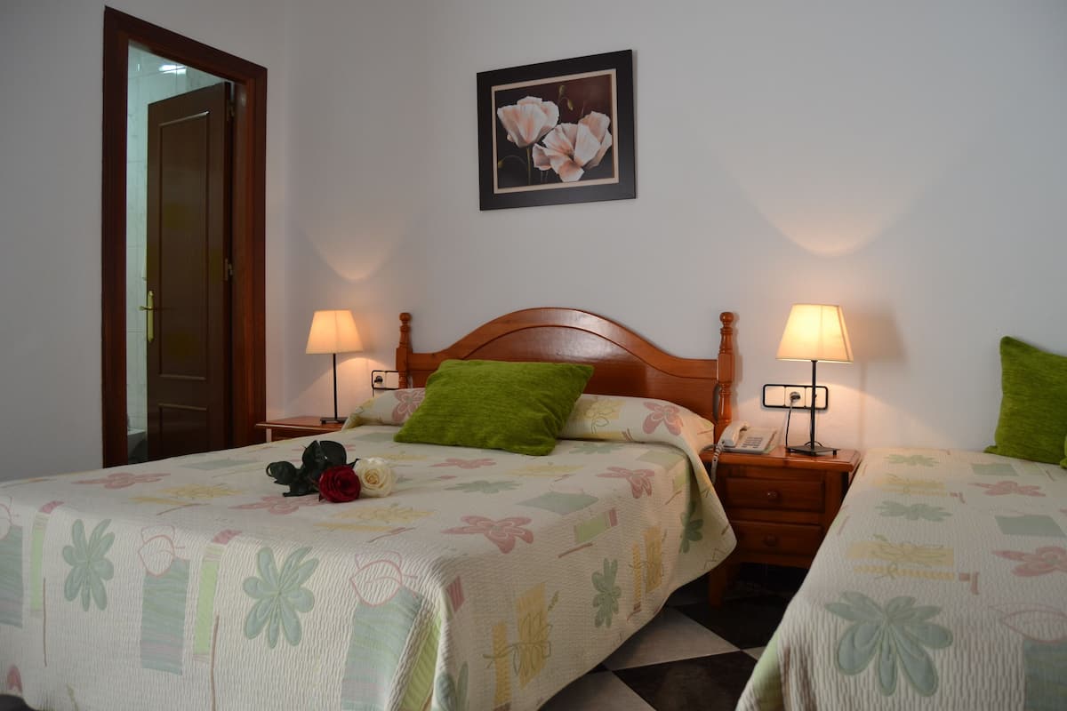 A hotel room with two beds, each with a floral bedspread, a green pillow, and a bedside lamp. There is a framed picture on the wall above the beds.