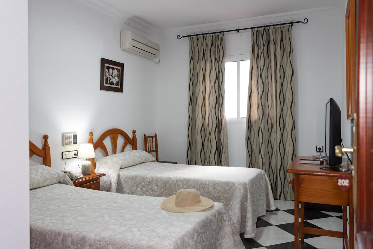 A hotel room with two beds, a bedside table with a lamp, a TV, and a wardrobe.