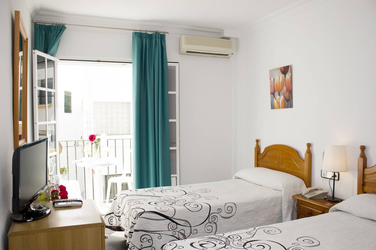A hotel room with two beds, a desk with a computer and a phone, a window with curtains, and an air conditioning unit.