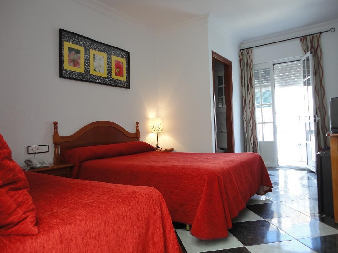 A hotel room with two beds, a wooden headboard, a nightstand with a lamp, a painting on the wall, and a check-in counter.
