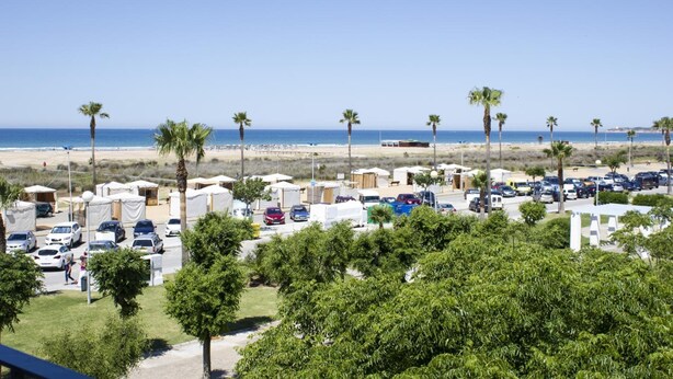 A beachside parking lot with several cars, tents, and palm trees. - Hotel Oasis (Conil de la Frontera)