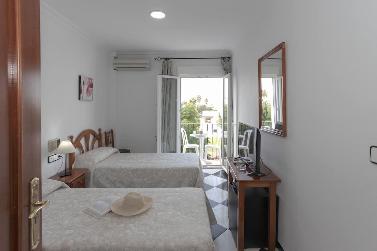 A hotel room with two beds, a desk with a computer, a mirror, and a view of the outside balcony.