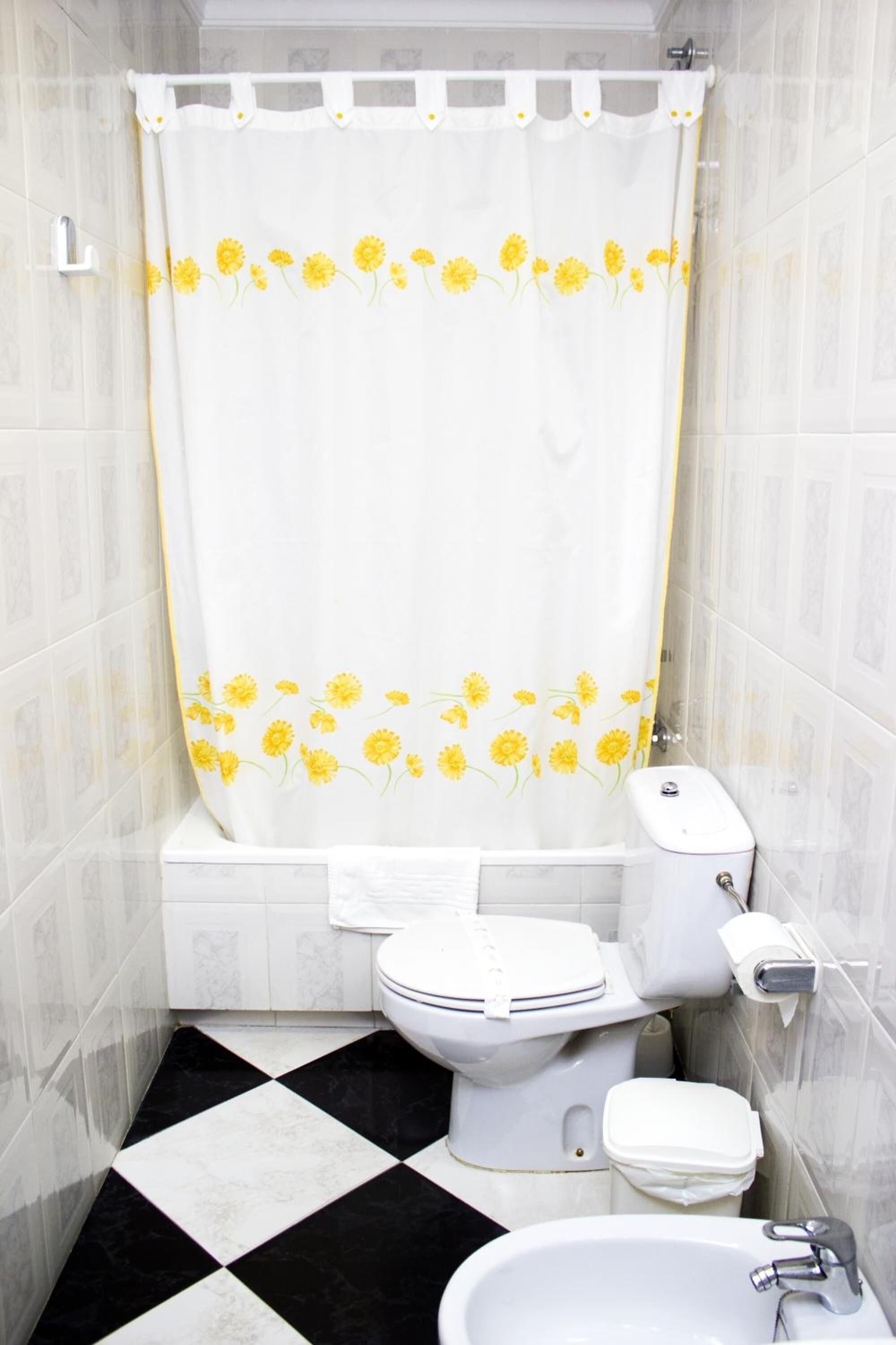 A bathroom with a white toilet, a sink, and a shower curtain with yellow flowers. The floor has a black and white checkered pattern.