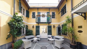 A courtyard with wicker furniture, potted plants, and a central door. - Manuelina Taste Hotel (Recco)