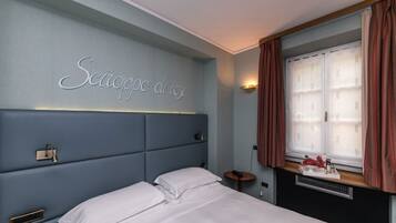 A bedroom with a bed, a bedside table, a nightstand, a wall-mounted light, a window with curtains, and a wall sign.