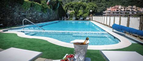 A pool area with a clear view of the water, a bottle of champagne, and a bowl of fruit on a table.