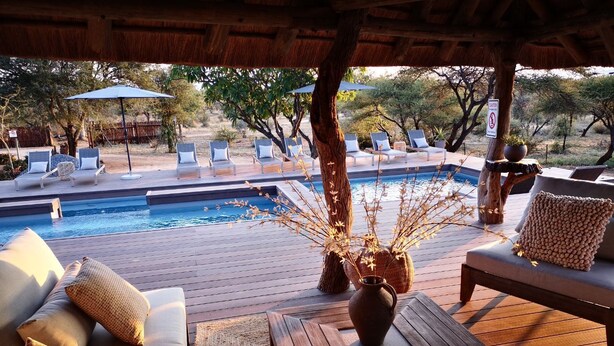 Zona junto a la piscina con sillas de descanso, una mesa de madera y un jarrón decorativo.