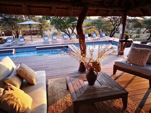 A poolside area with lounge chairs, a wooden table, and a decorative vase. - Tshukudu Game Lodge (Hoedspruit)