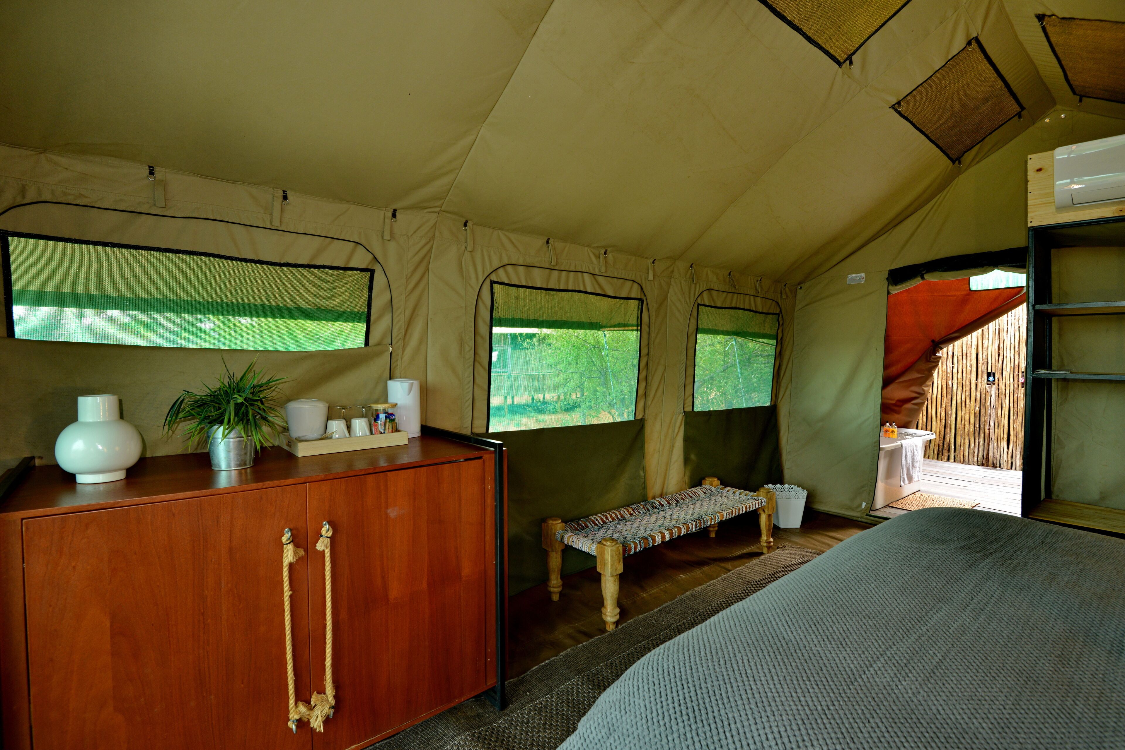 A tented room with a wooden cabinet, a bench, and a bed.