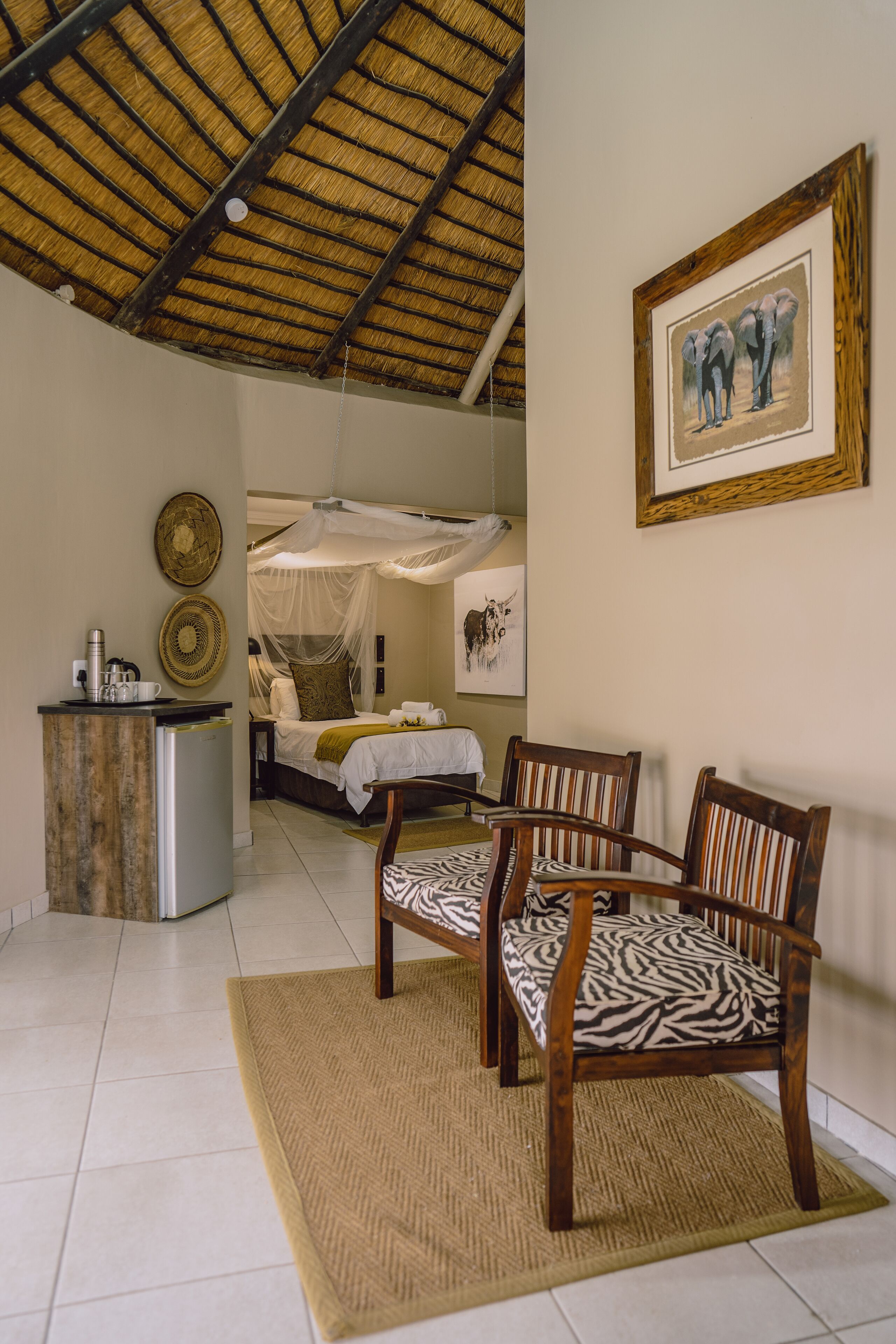 A room with a bed, a desk, and a chair. There is a picture on the wall and a mosquito net over the bed.