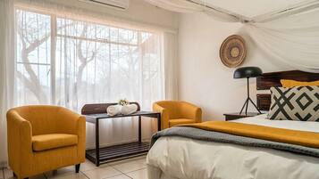 Habitación de hotel con una cama, dos sillones, una mesita con toallas, una lámpara de noche y un adorno en la pared.