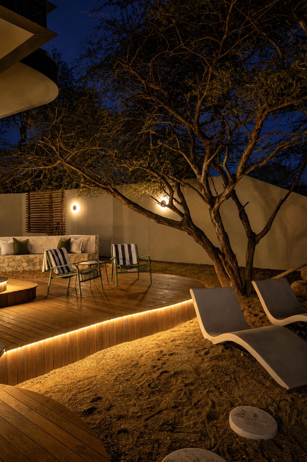 An outdoor seating area with lounge chairs and a fire pit, surrounded by a wooden deck and a sandy area.