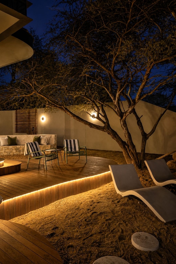 An outdoor seating area with lounge chairs and a fire pit, surrounded by a wooden deck and a sandy area. - Tshukudu Game Lodge (Hoedspruit)