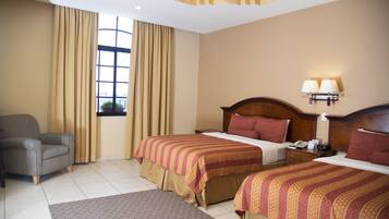 A hotel room with two beds, a chair, a nightstand, and a window with curtains.