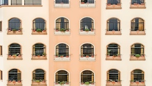 A building facade with multiple arched windows, each with a balcony and potted plants. - Monteolivos (San Pedro Sula)