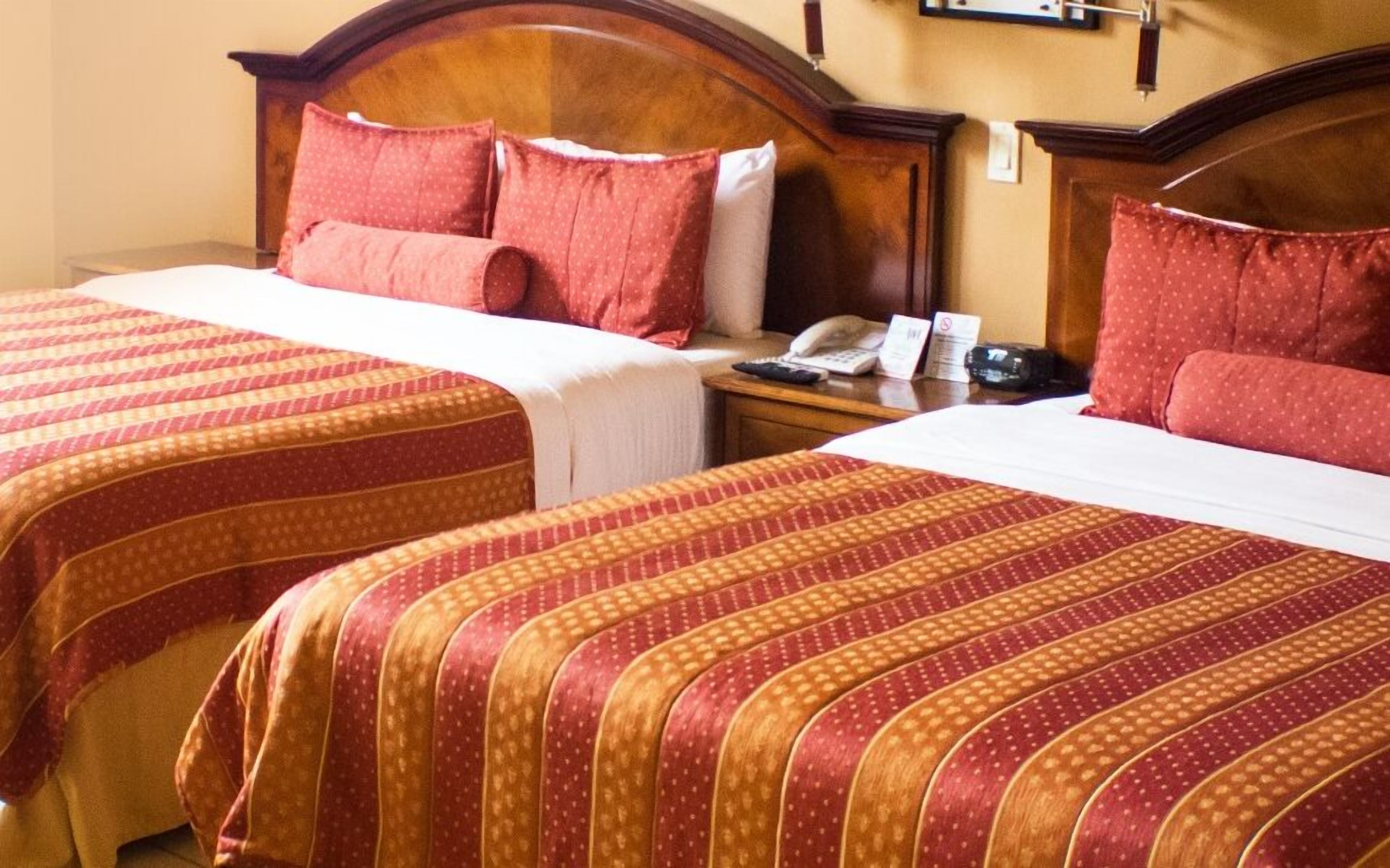 Two double beds with red and gold striped bedding, wooden headboards, and a nightstand with a phone and a sign.