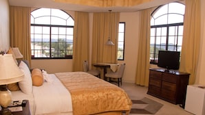 A hotel room with a large bed, a desk, a chair, a television, and a small refrigerator. - Monteolivos (San Pedro Sula)