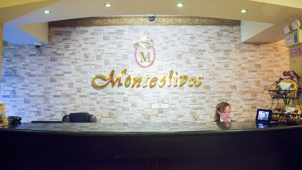 A reception desk with a stone wall backdrop and a logo. - Monteolivos (San Pedro Sula)