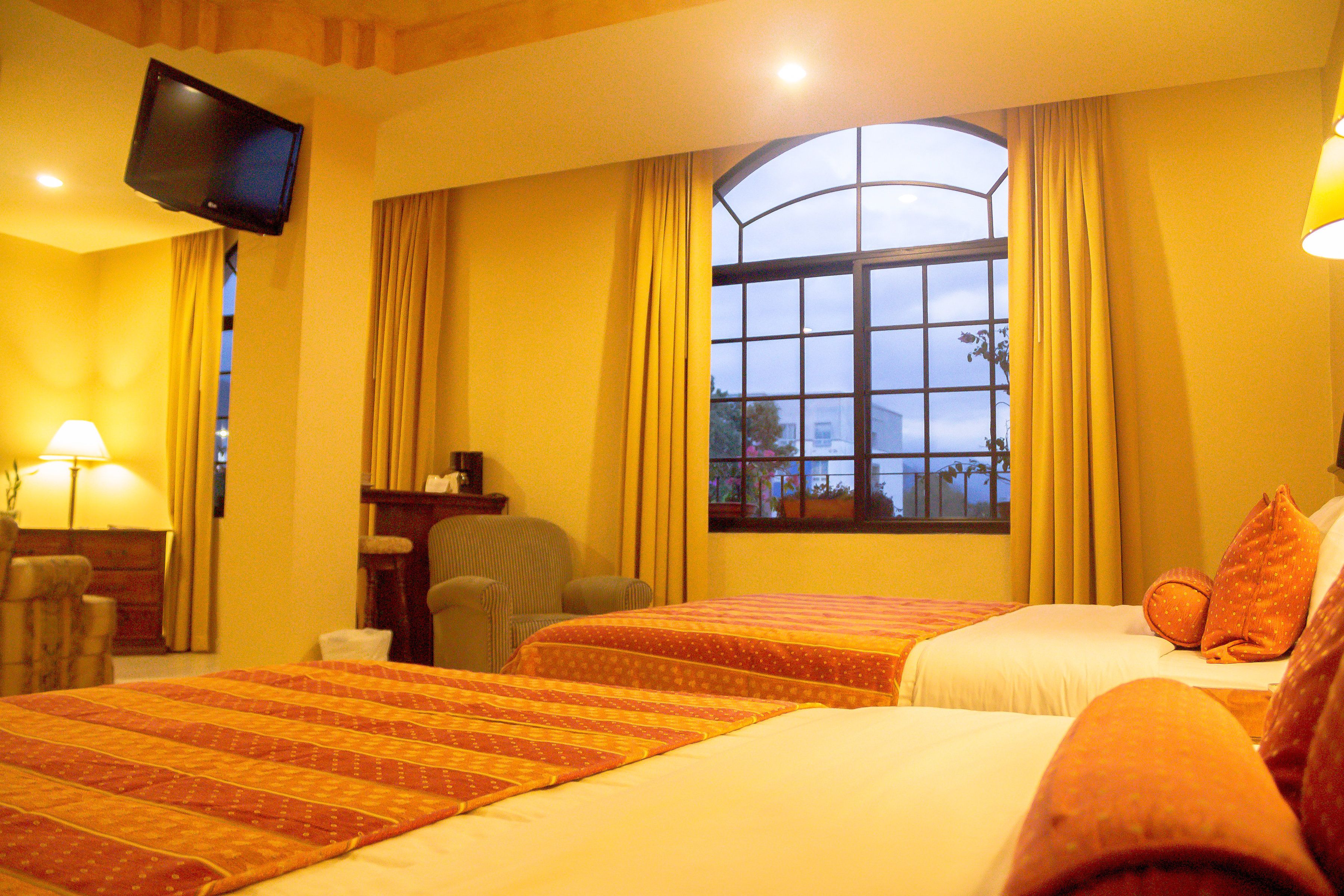 A hotel room with two beds, a television mounted on the wall, a window with curtains, and a chair.