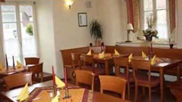 Uma sala de jantar com mesas e cadeiras de madeira, um candelabro e uma janela com cortinas.