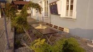 A narrow courtyard with a wooden table and chairs, surrounded by greenery and a stone wall. - Hotel Schwarzacher Hof (Schwarzach)