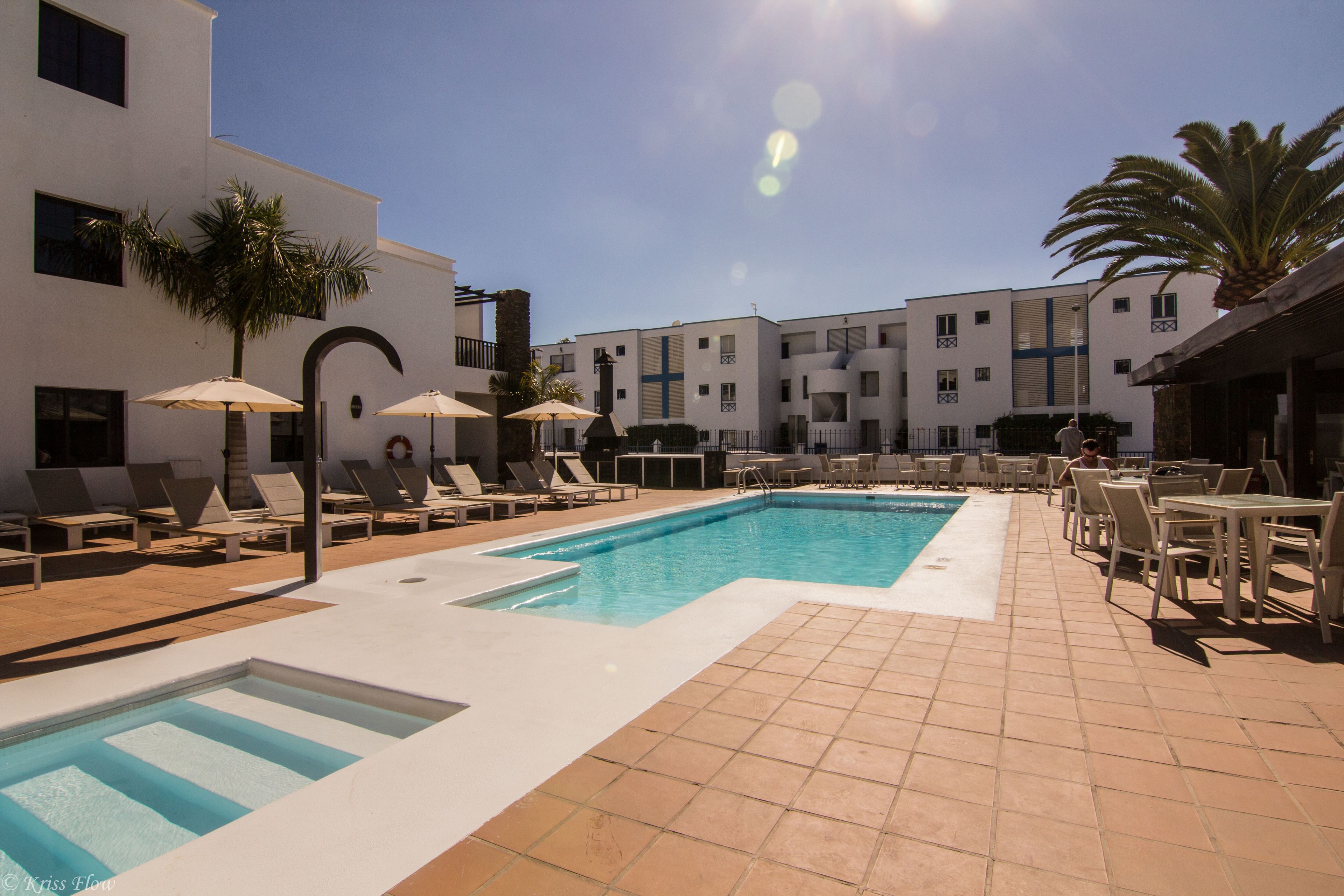 A pool area with lounge chairs and umbrellas, surrounded by a building with multiple balconies.
