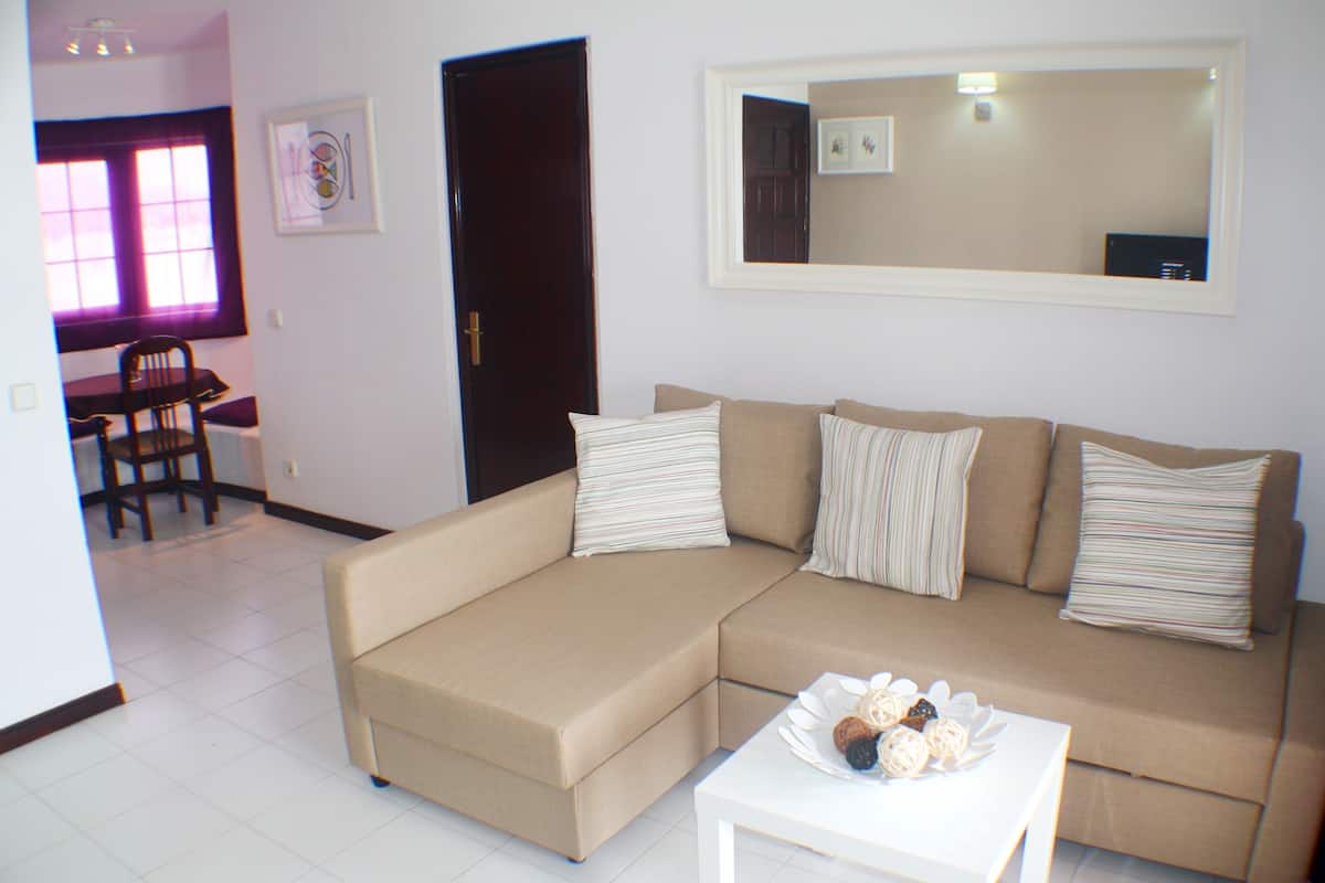 A living room with a beige sectional sofa, a white coffee table, and a dining area with a wooden table and chairs.