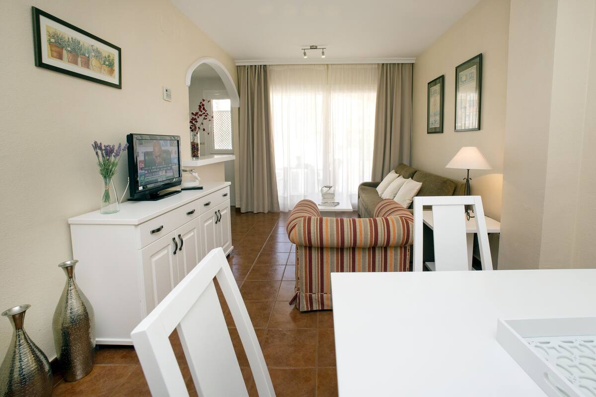 Una habitación de hotel con televisión, una mesa de comedor, un sofá y una lámpara.