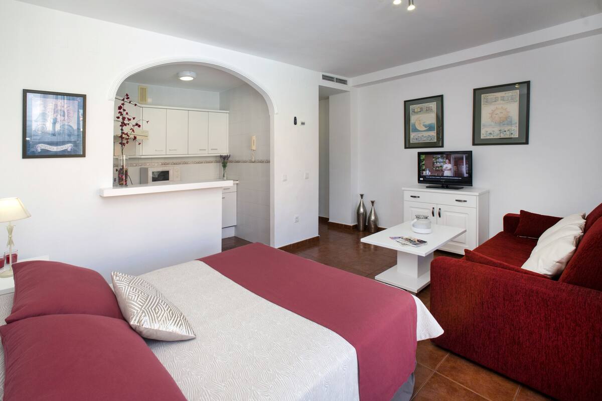 Una habitación de hotel con dos camas, una kitchenette pequeña, un televisor y una mesa de comedor.