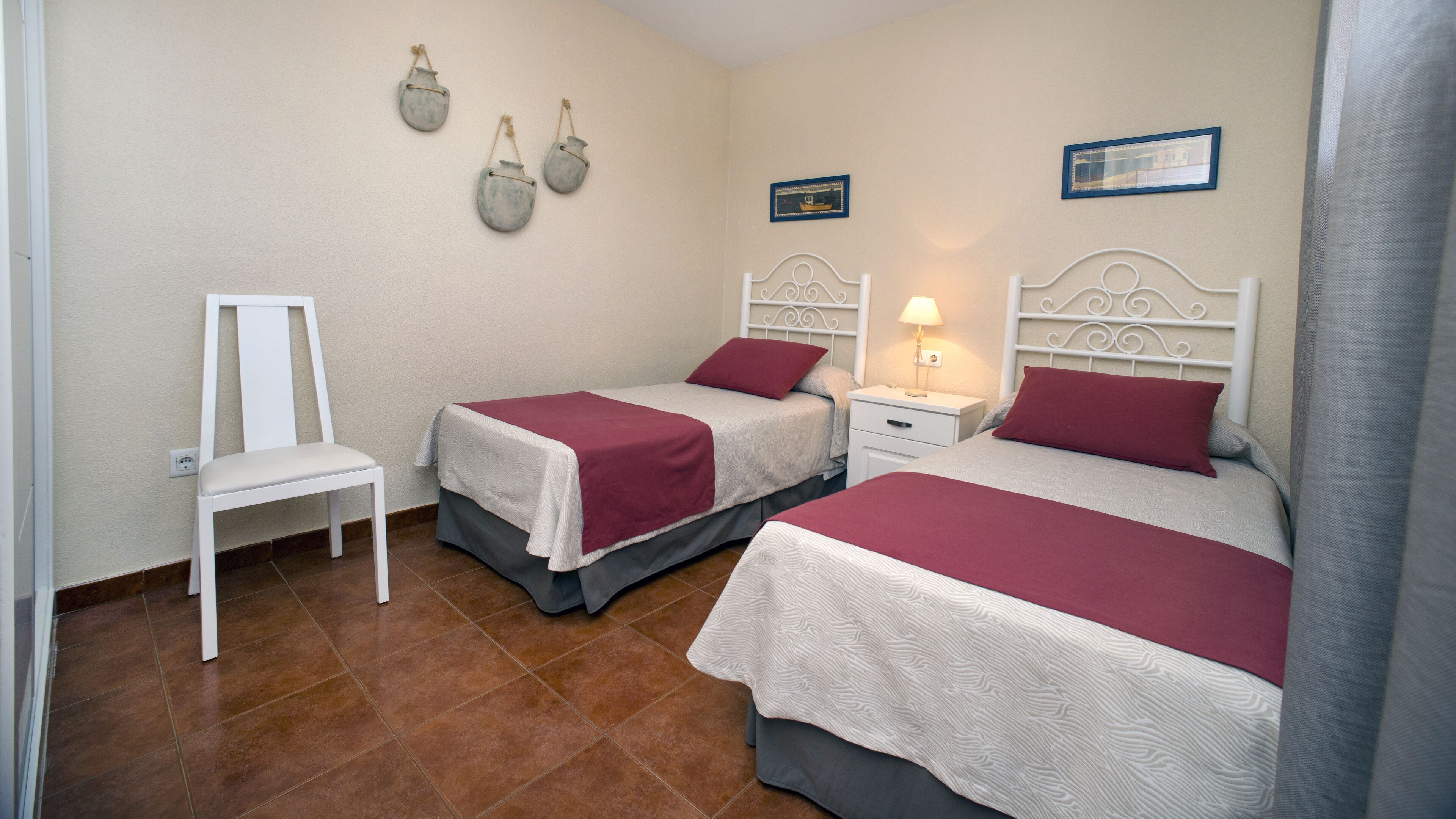Un dormitorio con dos camas, una silla y una mesita de noche con lámpara.