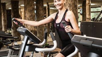 A gym with treadmills, a woman using one, and wooden pillars.