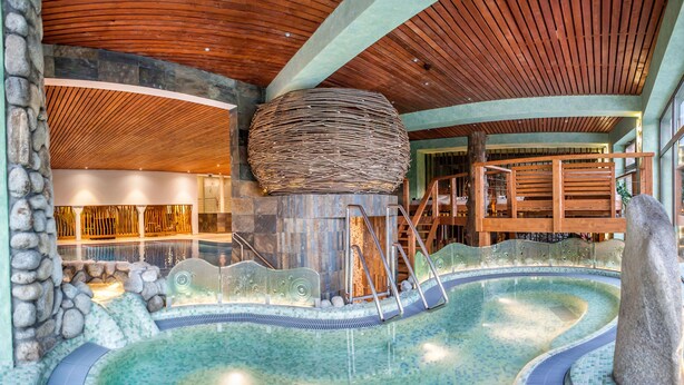 Uma área de spa com hidromassagem, parede de pedra e teto de madeira.