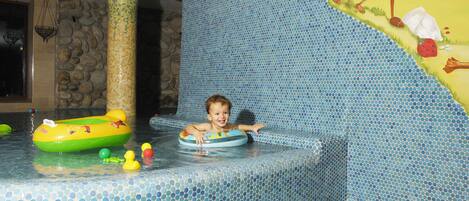 A child in a pool with a green inflatable ring, surrounded by toys.