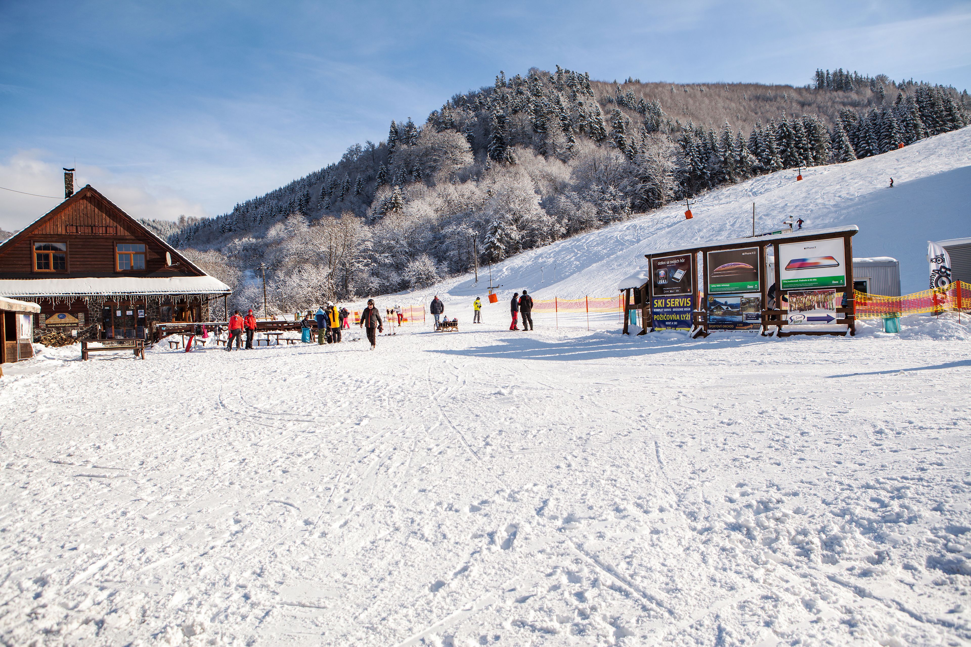 Un bâtiment en bois doté d’un porche abrité, d’un télésiège et d’un point de service pour les équipements de ski, situé sur une pente enneigée.