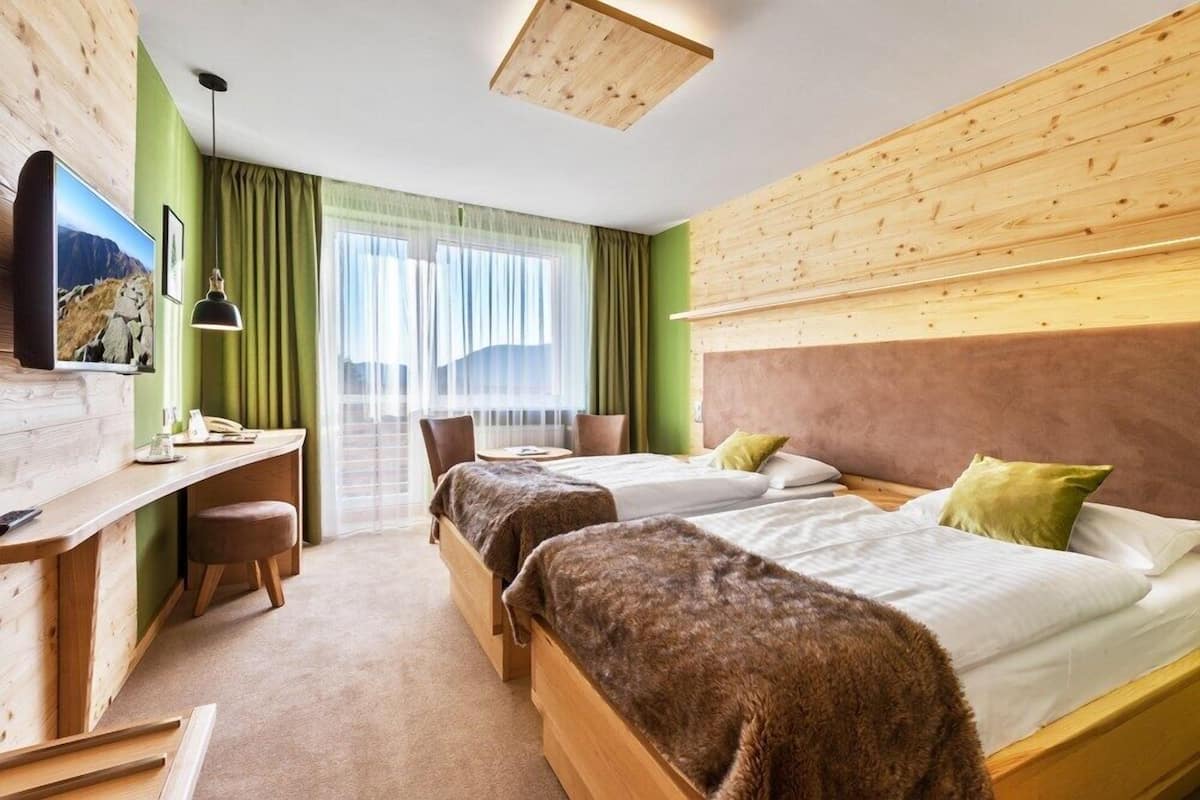A hotel room with two beds, a desk, a TV, and a view of the mountains.