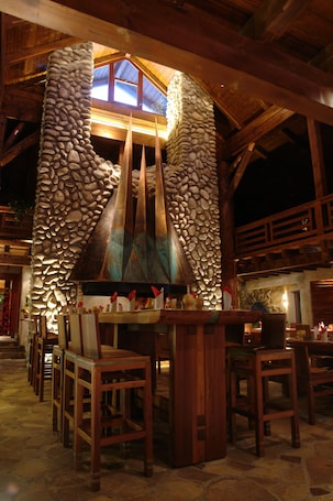 A stone fireplace with a chimney, wooden chairs, and a bar area in a rustic interior.