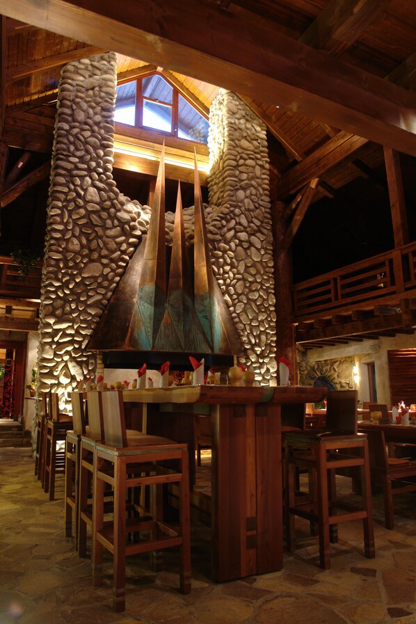 Una chimenea de piedra con chimenea, sillas de madera y una zona de bar en un interior rústico.
