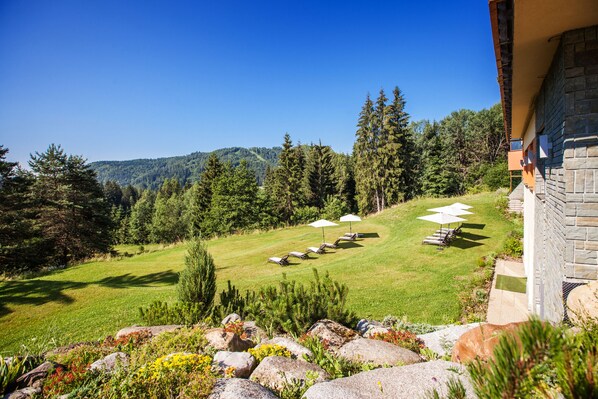 A landscaped garden with a lawn, seating area, and a view of a forested hill.