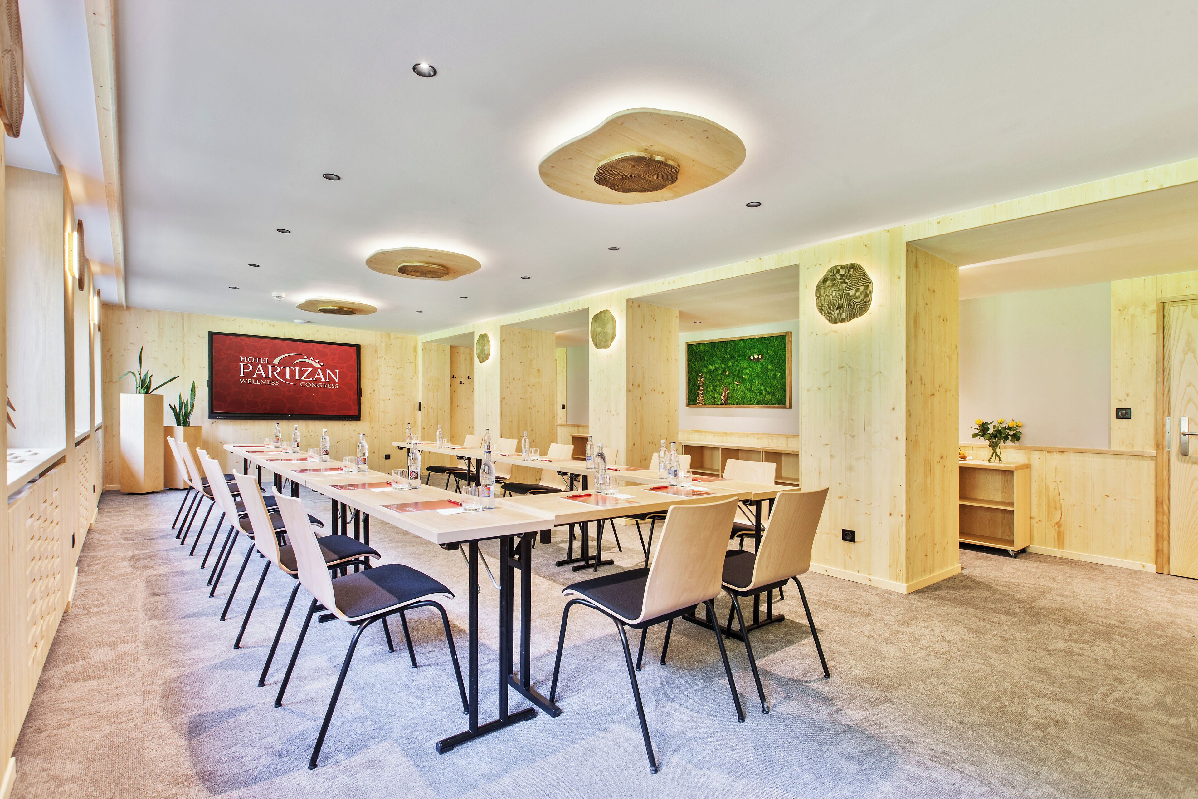 A conference room with a long table, chairs, and a screen displaying 'Hotel Partizan Wellness Congress'.