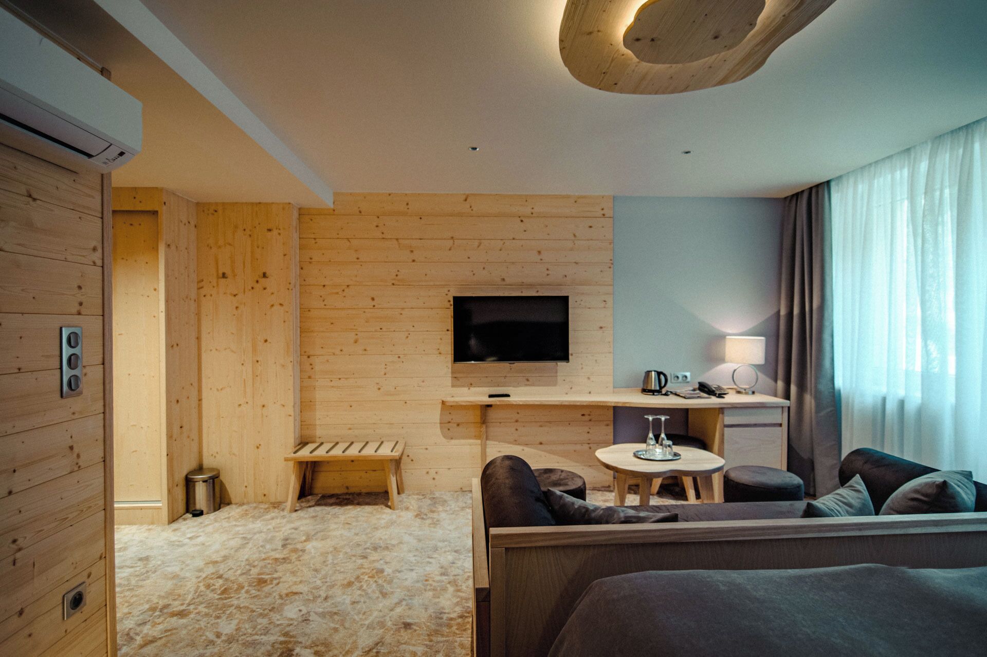 Una habitación de hotel moderna con detalles de madera, un televisor de pantalla plana, una mesita redonda y un sofá.